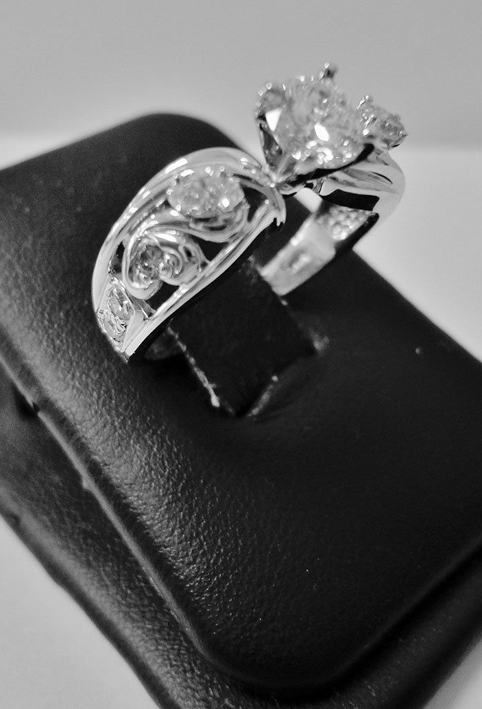 Two silver rings with clear gemstones on a black jewelry display stand