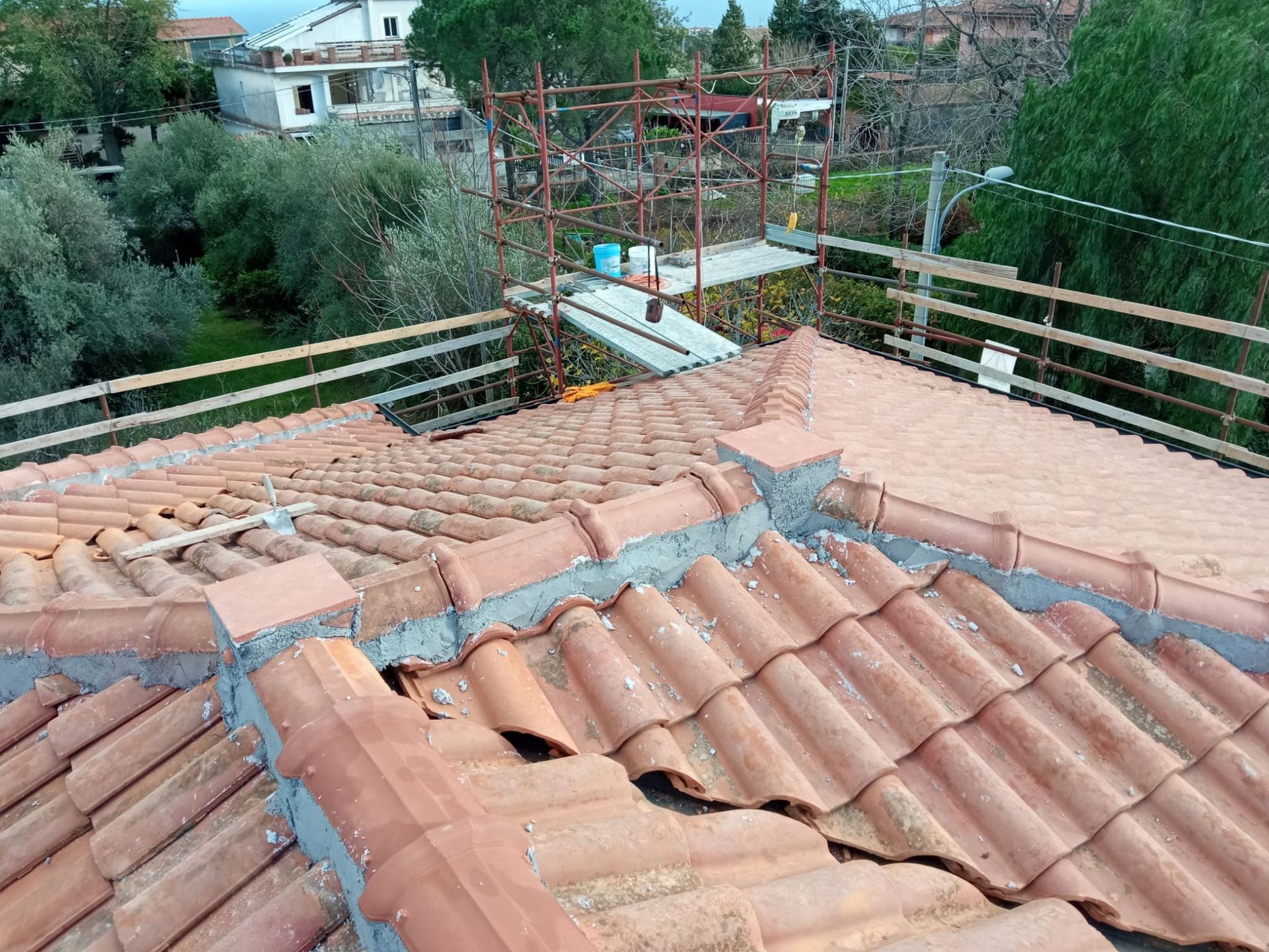 Tegole di terracotta danneggiate con struttura metallica e alberi sullo sfondo.