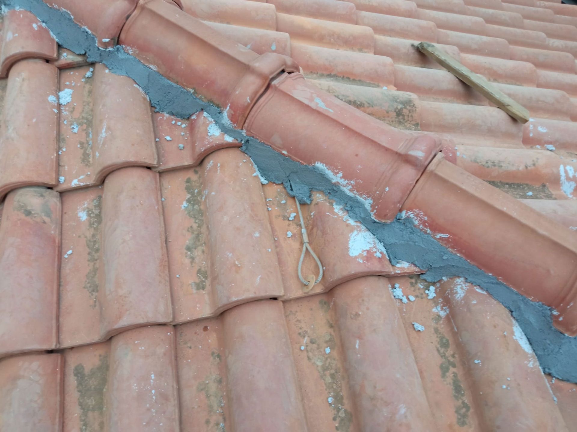 Tetto di tegole rosse danneggiato con colmo crepato riparato con materiale di riparazione grigio-blu.