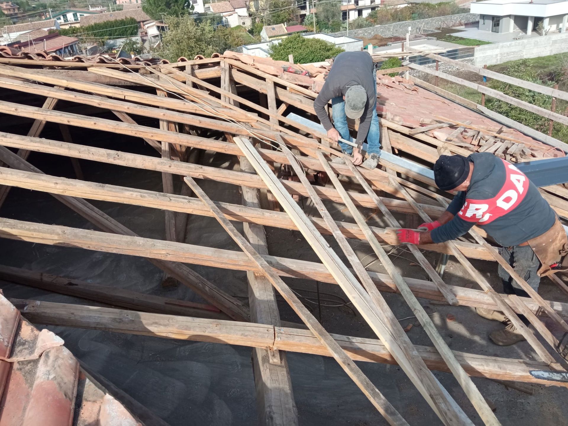 Operai intenti a riparare una struttura di tetto in legno danneggiata, con assi e travi esposte all'esterno.