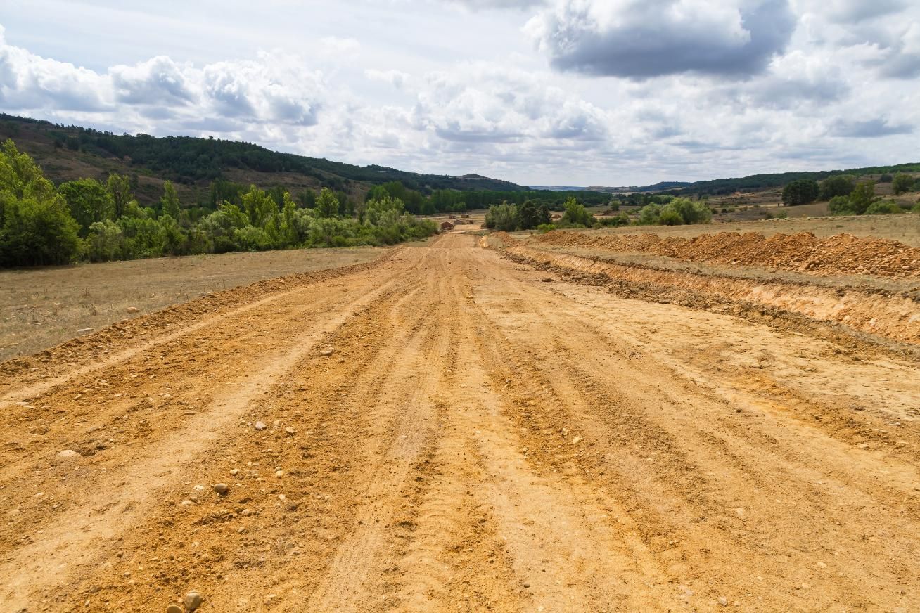 Wide dirt road through a rural landscape under cloudy skies
