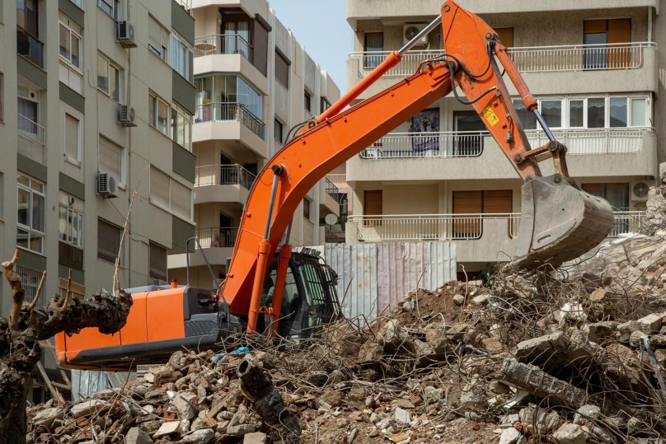 Orange excavator digging rubble at a demolition site in front of apartment buildings