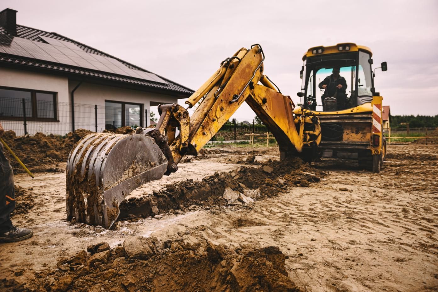 Yellow excavator digging muddy ground beside a house under construction