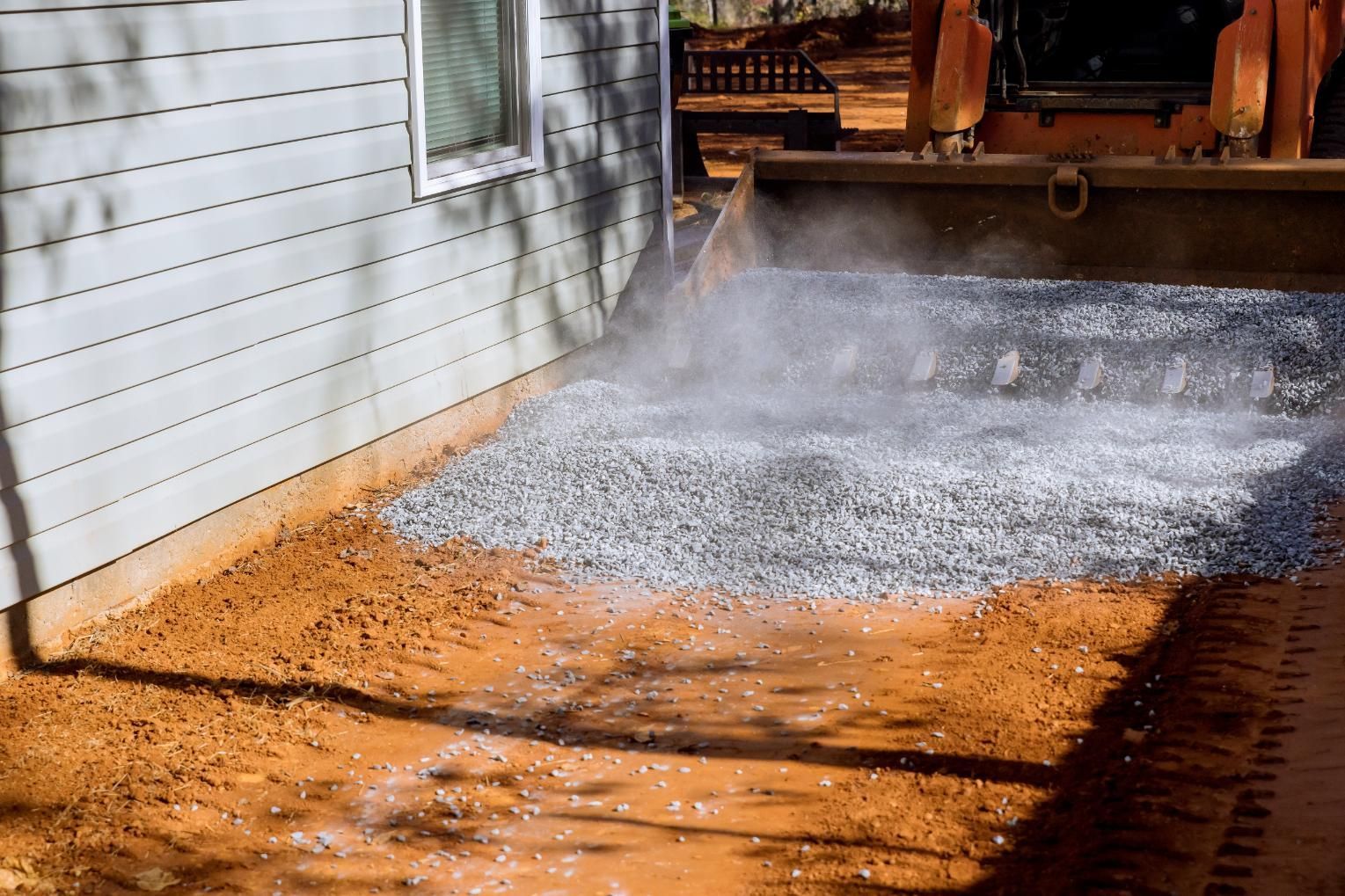 Construction machine spraying water over a dirt driveway beside a white house