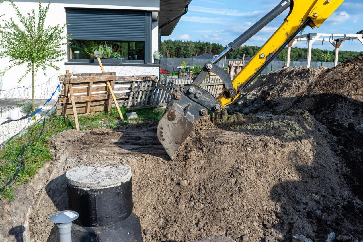 Excavator digging a large dirt pile beside a house and patio in a backyard construction area