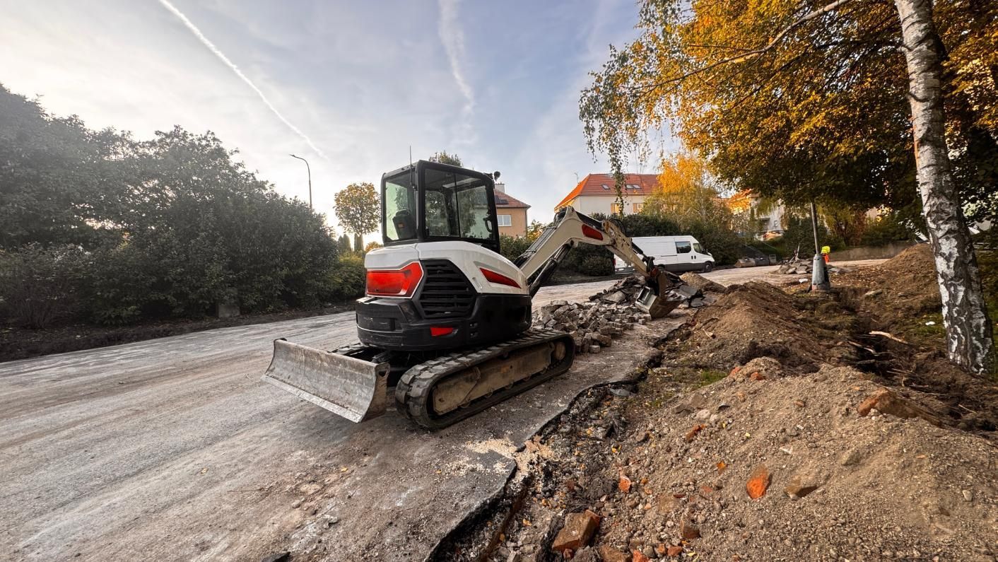 Excavator working beside a muddy road with trees and autumn leaves nearby