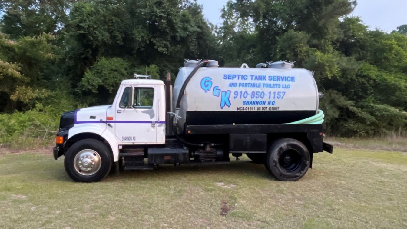 White and black utility truck with blue lettering parked on grass, side view with trees in the background