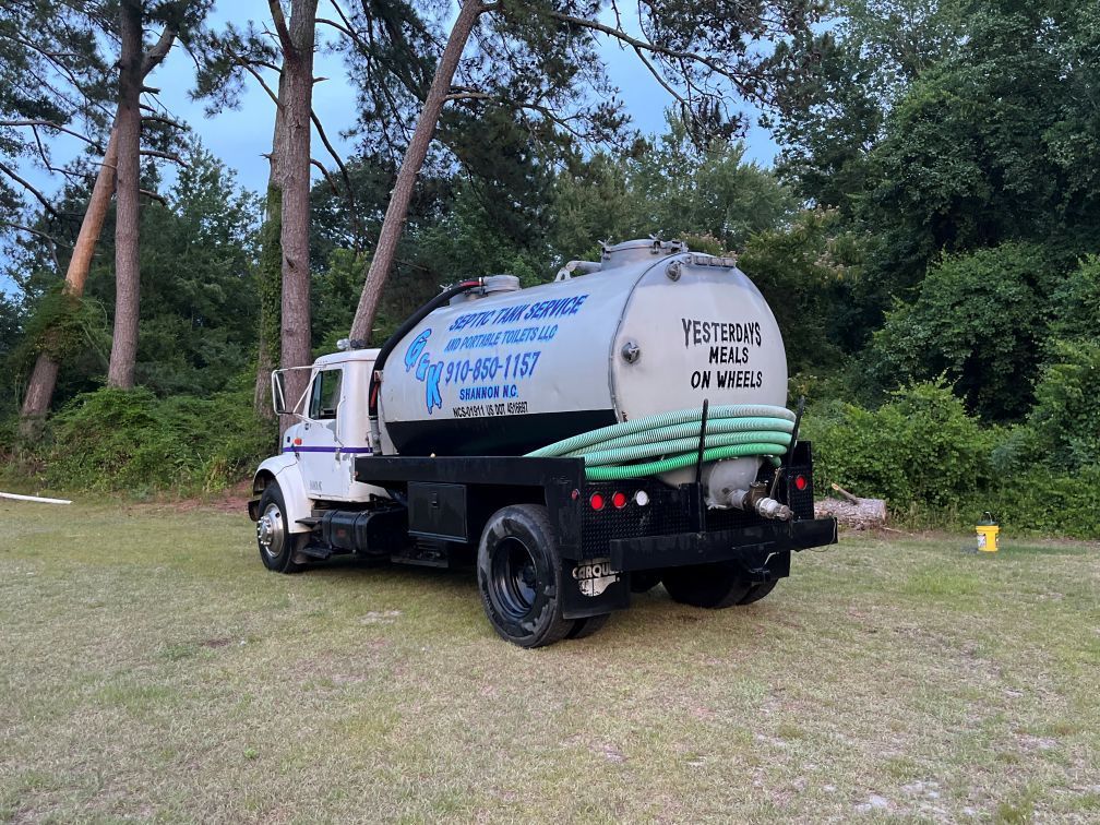 White septic tanker truck parked on grass near trees, with blue lettering on the tank in Aberdeen NC