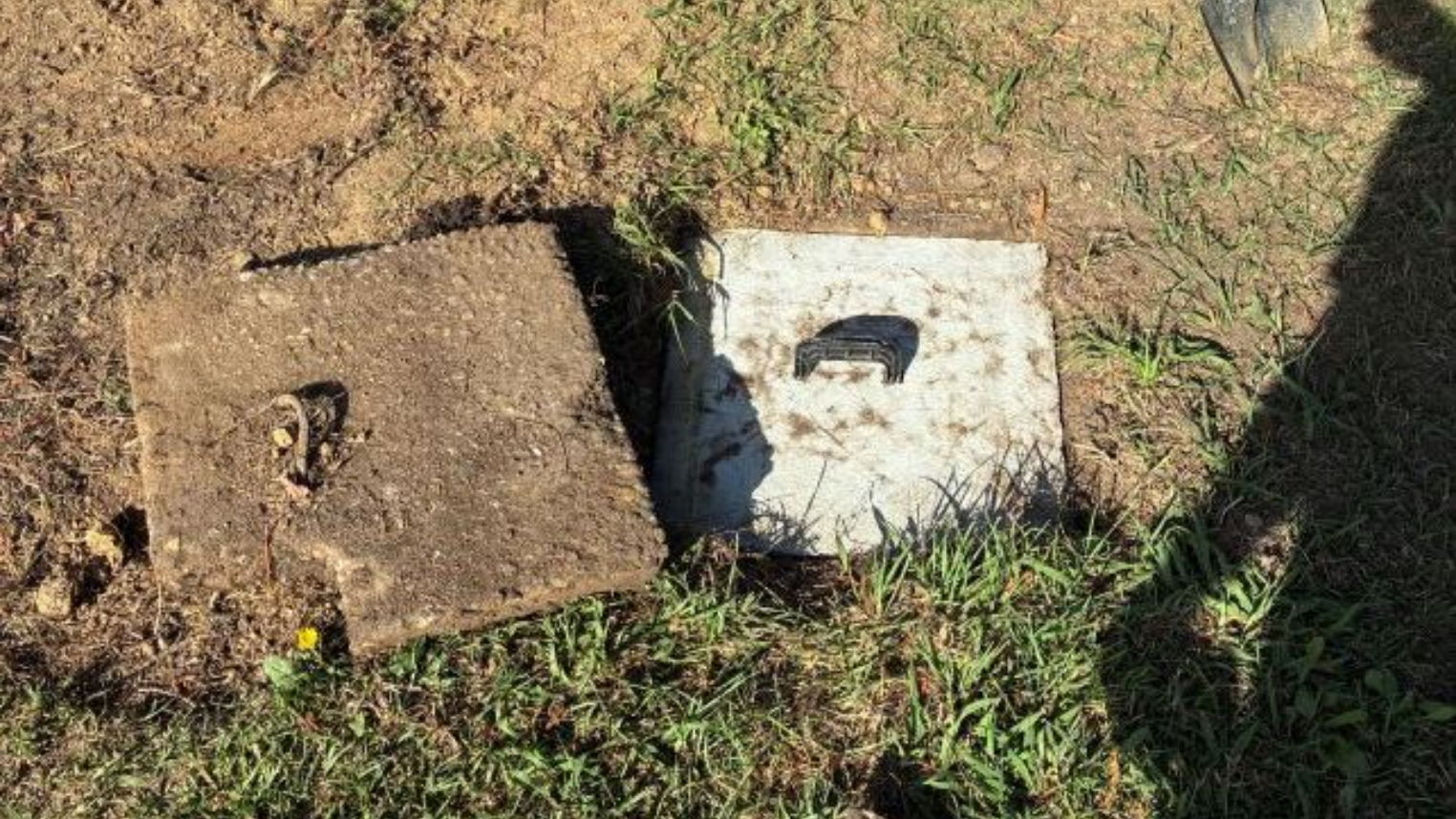 Two square concrete utility covers in dirt and grass, one brown and one white, with a shadow nearby
