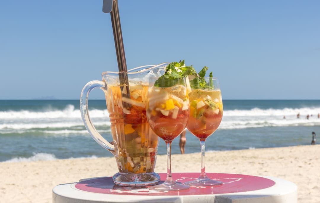 Dois copos de bebida estão sobre uma mesa na praia.