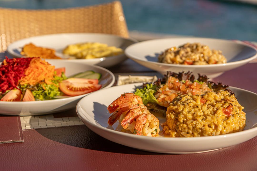 Uma mesa coberta com pratos de comida e uma piscina ao fundo.