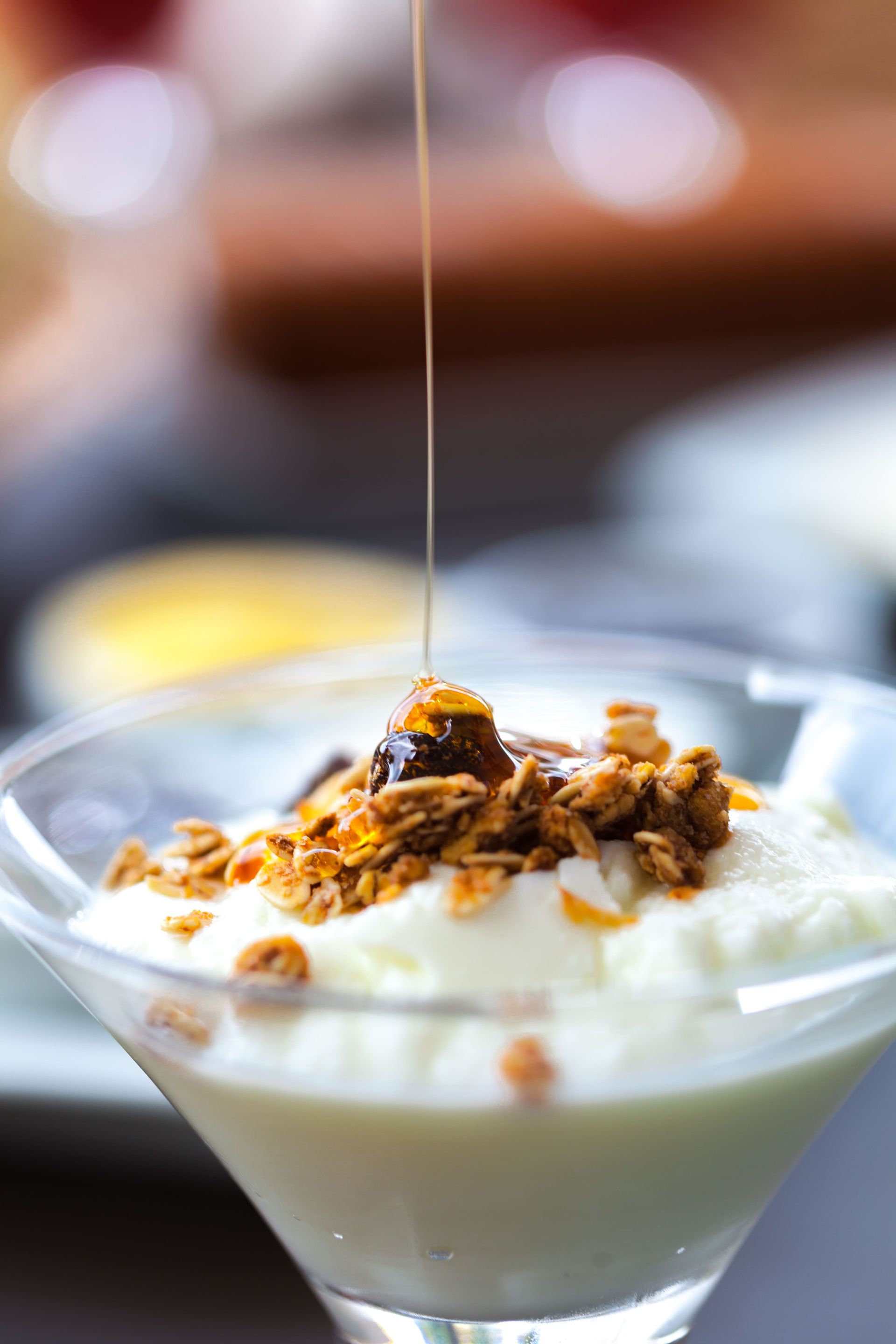 Uma taça de martini cheia de iogurte e granola com mel sendo derramado por cima