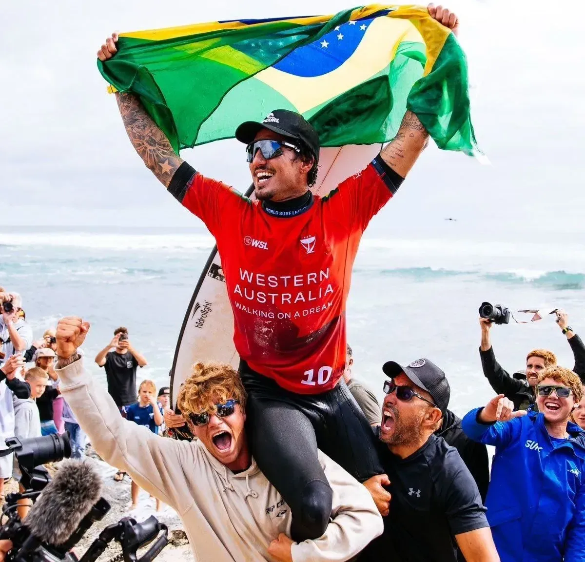 Gabriel Medina comemorando vitória no surfe com a bandeira do Brasil sobre a cabeça.