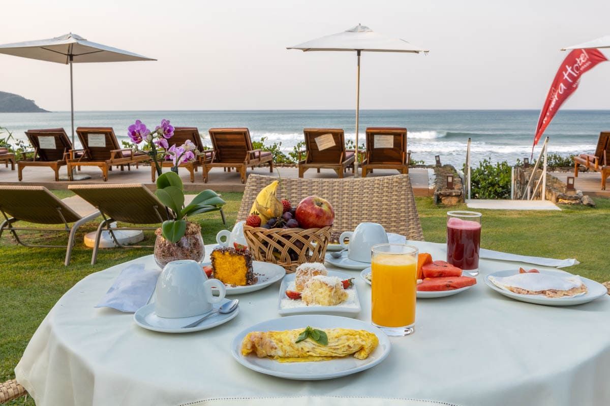 Uma mesa com pratos de comida e bebidas em frente ao oceano.