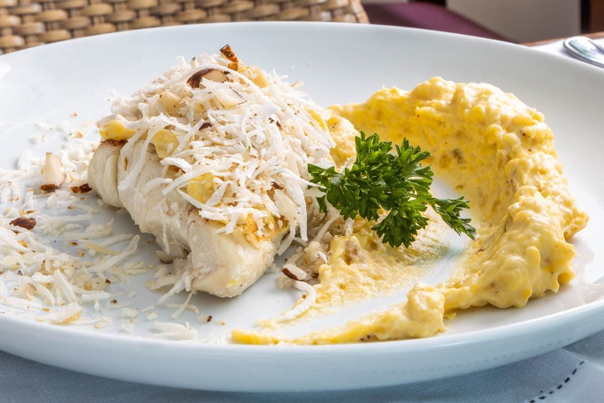 Um prato branco coberto com um pedaço de peixe e purê de batatas.