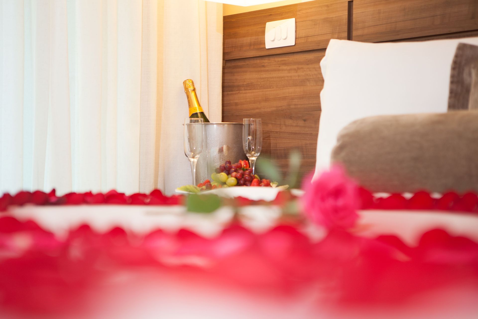 Um quarto de hotel decorado para o dia dos namorados com um balde de champanhe, rosas e frutas.