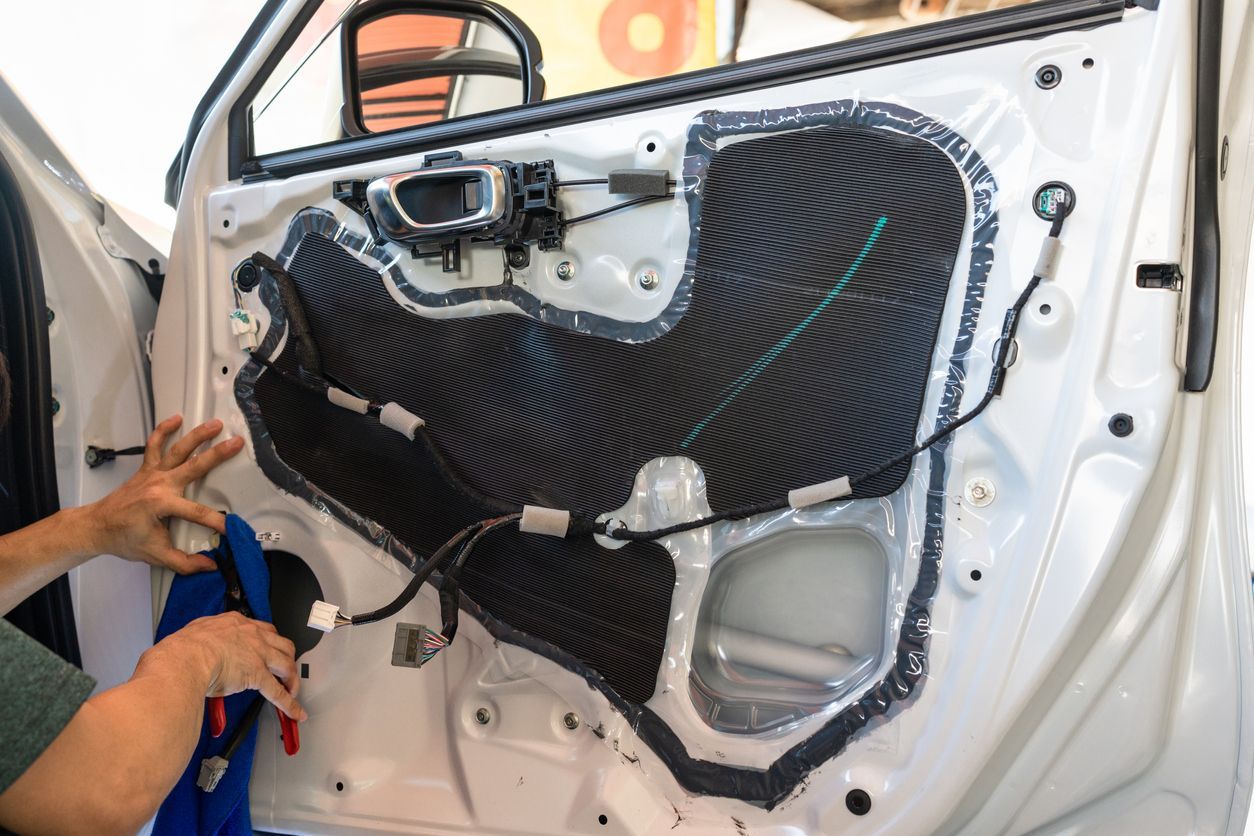 Car door interior disassembled, exposing wiring and insulation. A person works on the door.