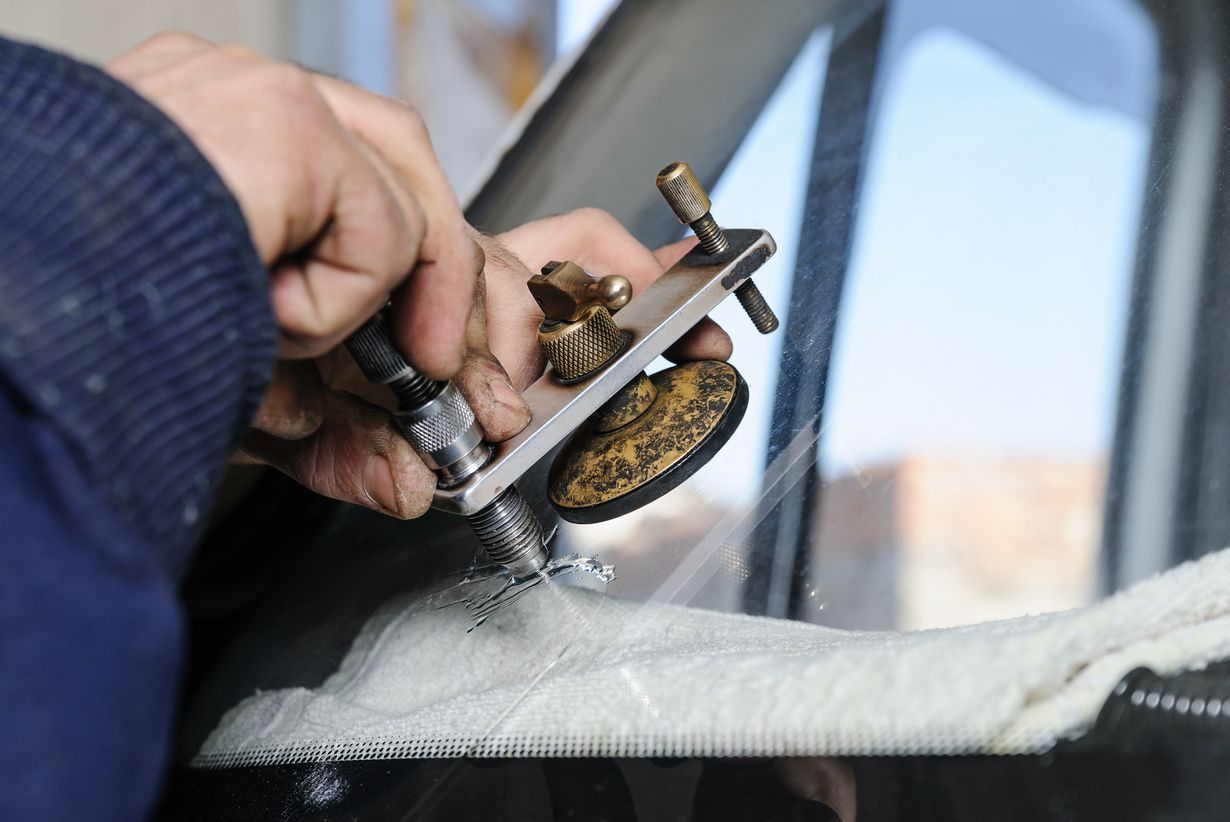 Person repairing windshield crack with a tool.