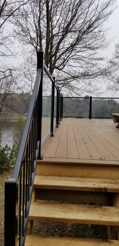 Une terrasse en bois avec des escaliers qui y mènent et une balustrade en verre.