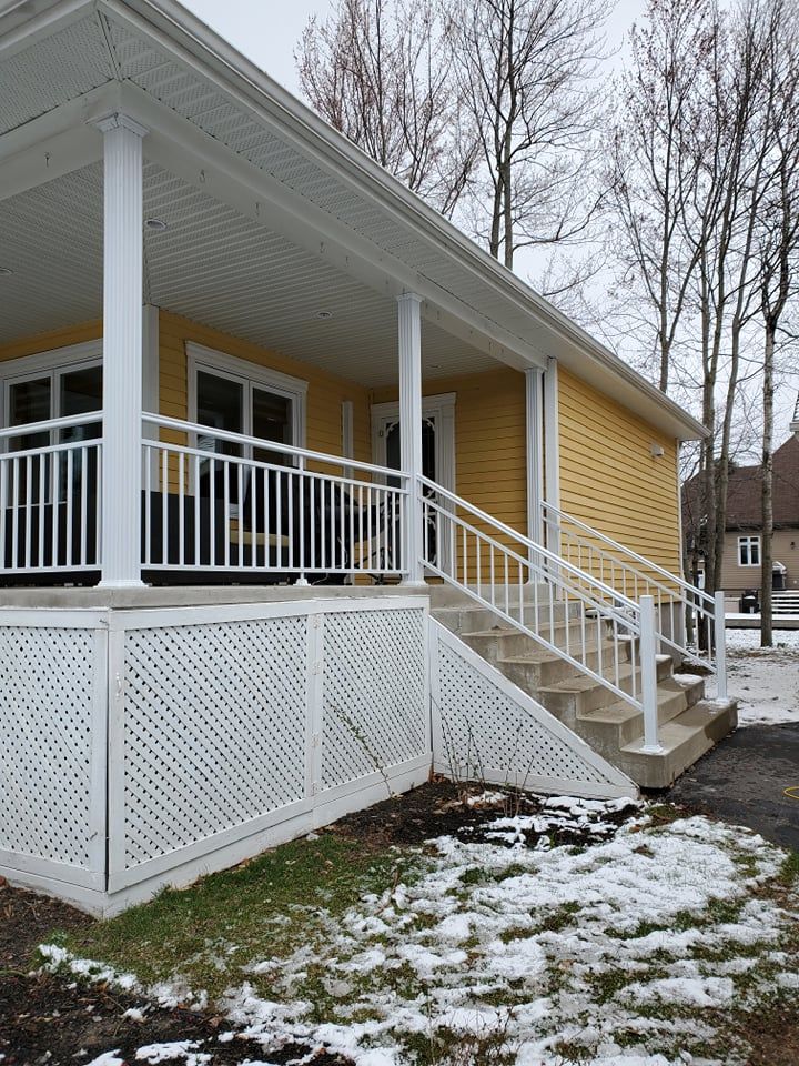 Une maison jaune avec une balustrade et des escaliers blancs