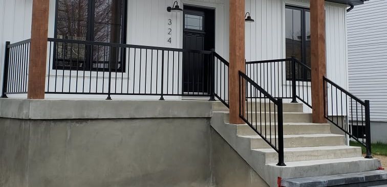 Vue extérieure d'une maison blanche avec une balustrade noire et des marches menant à la porte d'entrée.