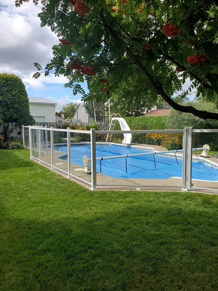 Une grande piscine entourée d'une clôture en verre dans une cour arrière.