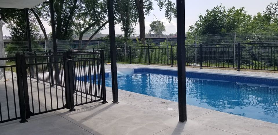 Une grande piscine avec une clôture autour et des arbres en arrière-plan.