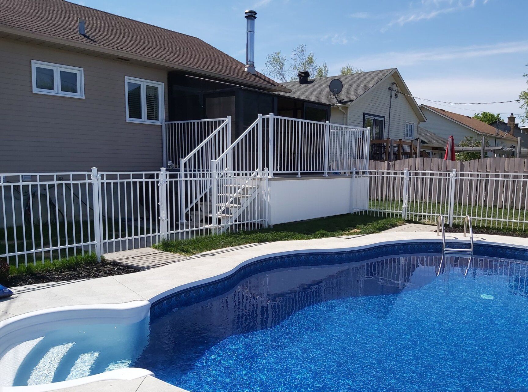 Jardin avec piscine, terrasse, clôture blanche et maison au toit marron.