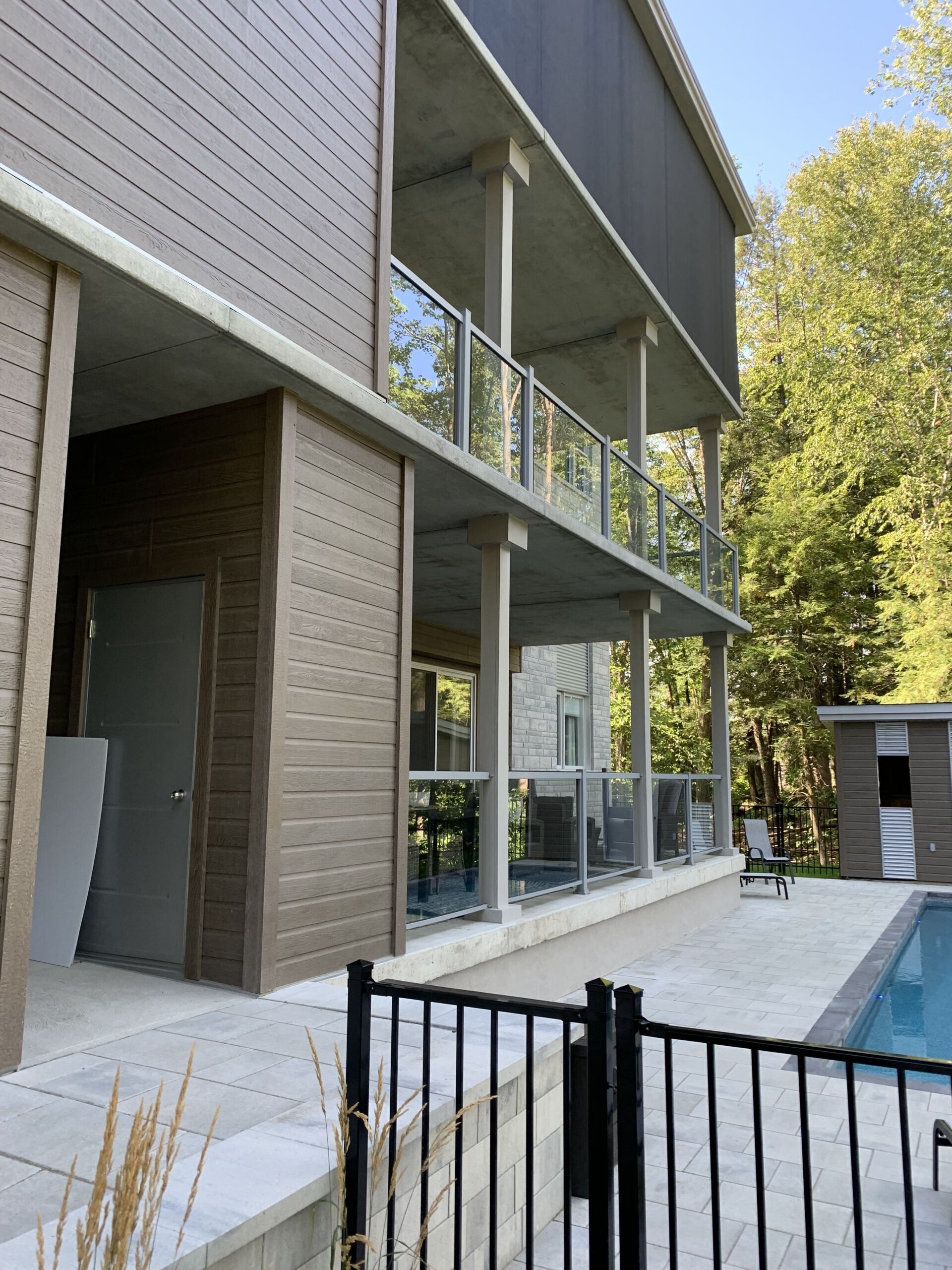Immeuble avec deux balcons en béton, des garde-corps en verre et un revêtement extérieur marron, situé près d'une piscine.