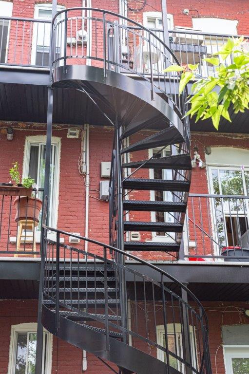 Escalier en colimaçon noir devant un bâtiment en briques rouges avec des fenêtres.