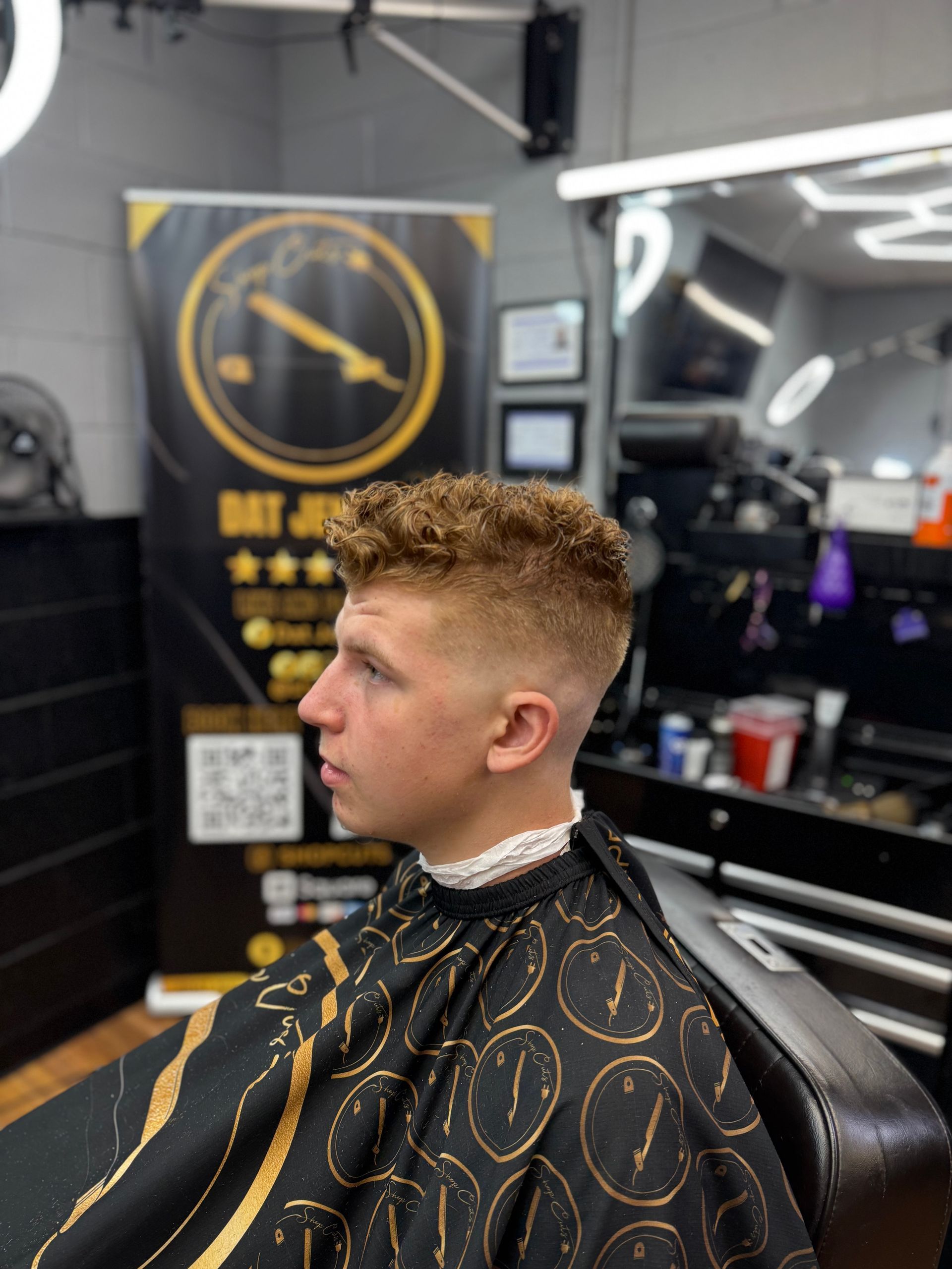 Side profile of a person with a short, curly-topped haircut featuring a clean skin fade in a barbershop.