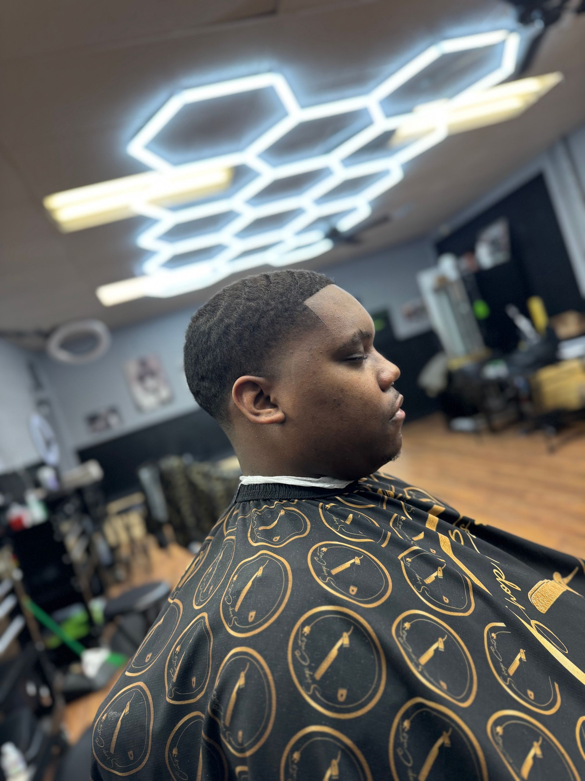 A person sits in a barber chair wearing a patterned cape, showcasing a fresh, close-cropped haircut in a salon.