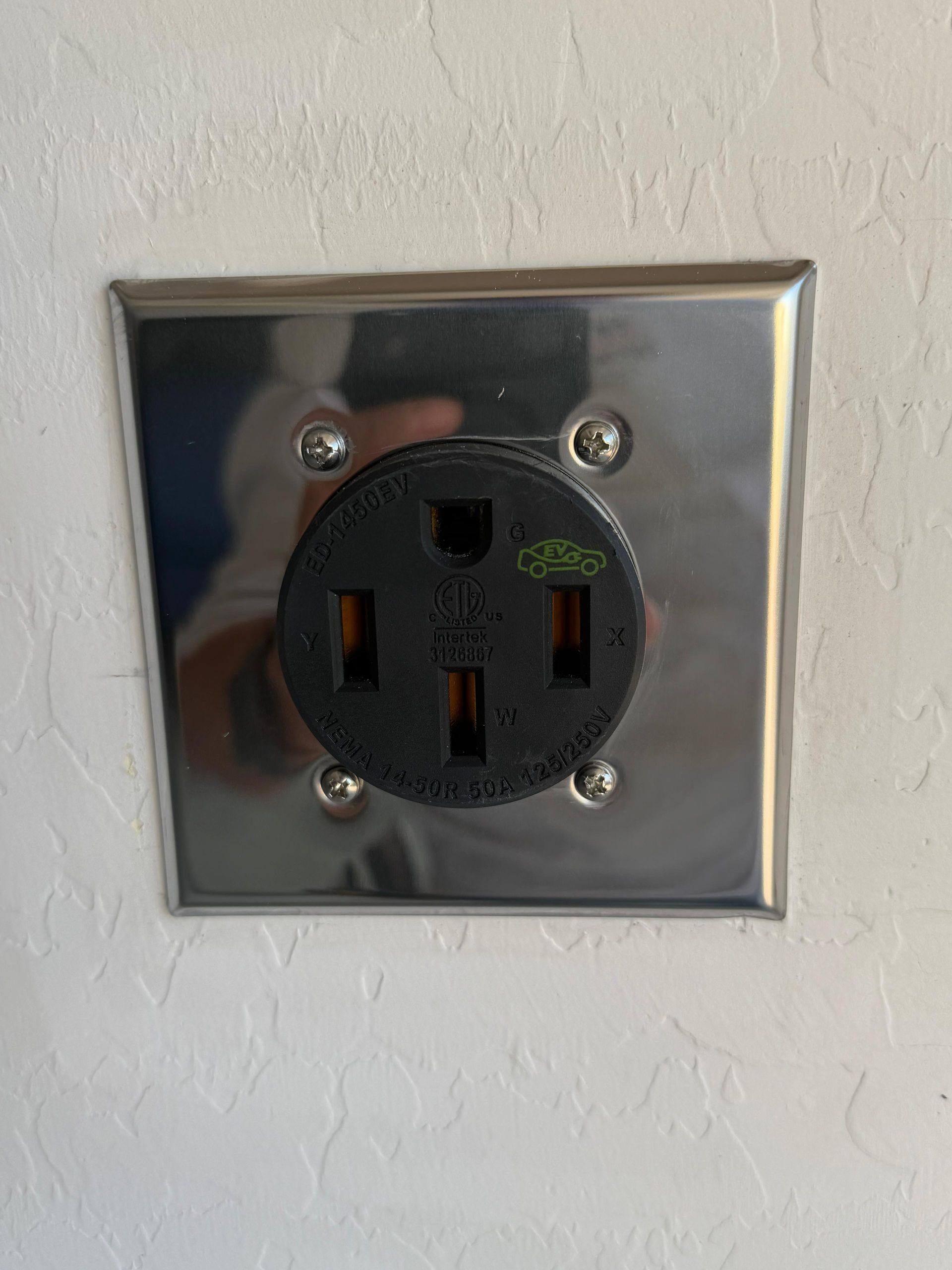 Chrome electric vehicle wall outlet with black faceplate and plug slots installed by For The People Electric.