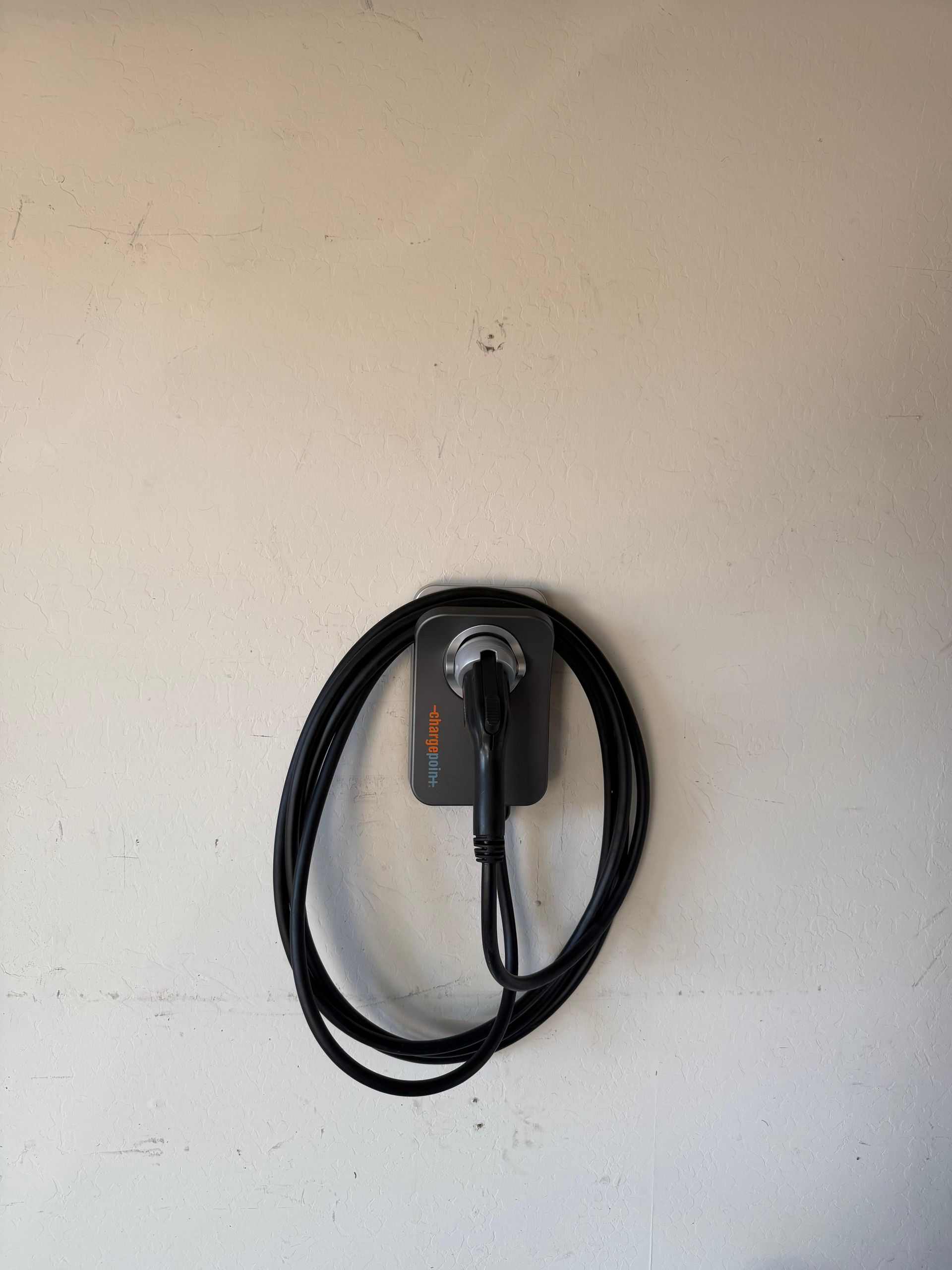 Black coiled cable hanging on a wall-mounted charger against a beige wall