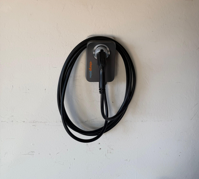 Coiled black charging cable hanging on a wall-mounted dock