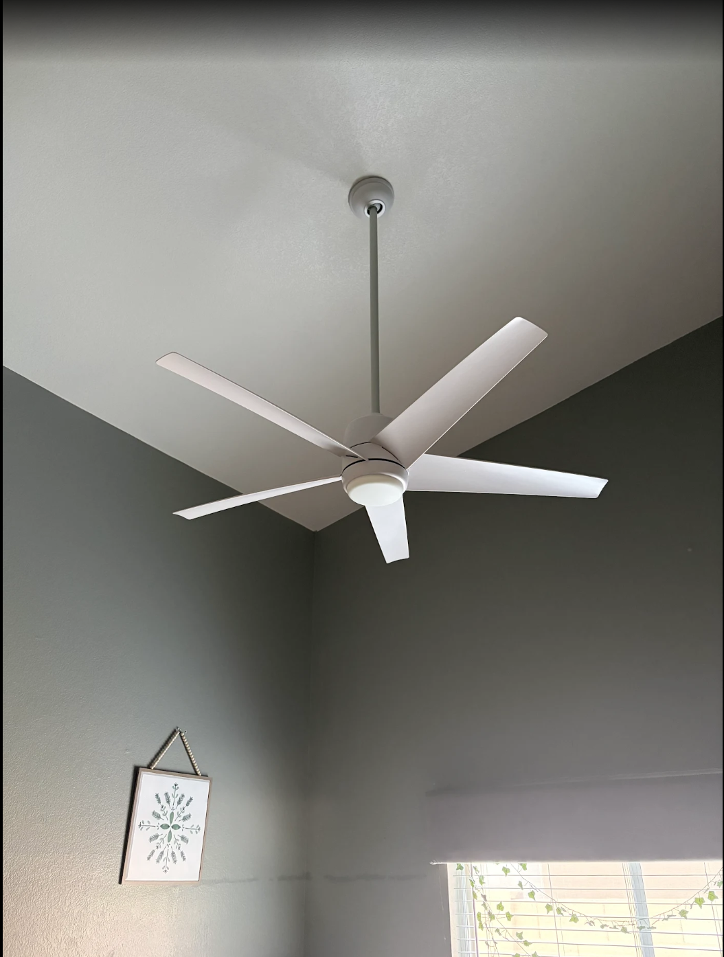 White ceiling fan on a gray wall and ceiling in a room with a small hanging sign and window below