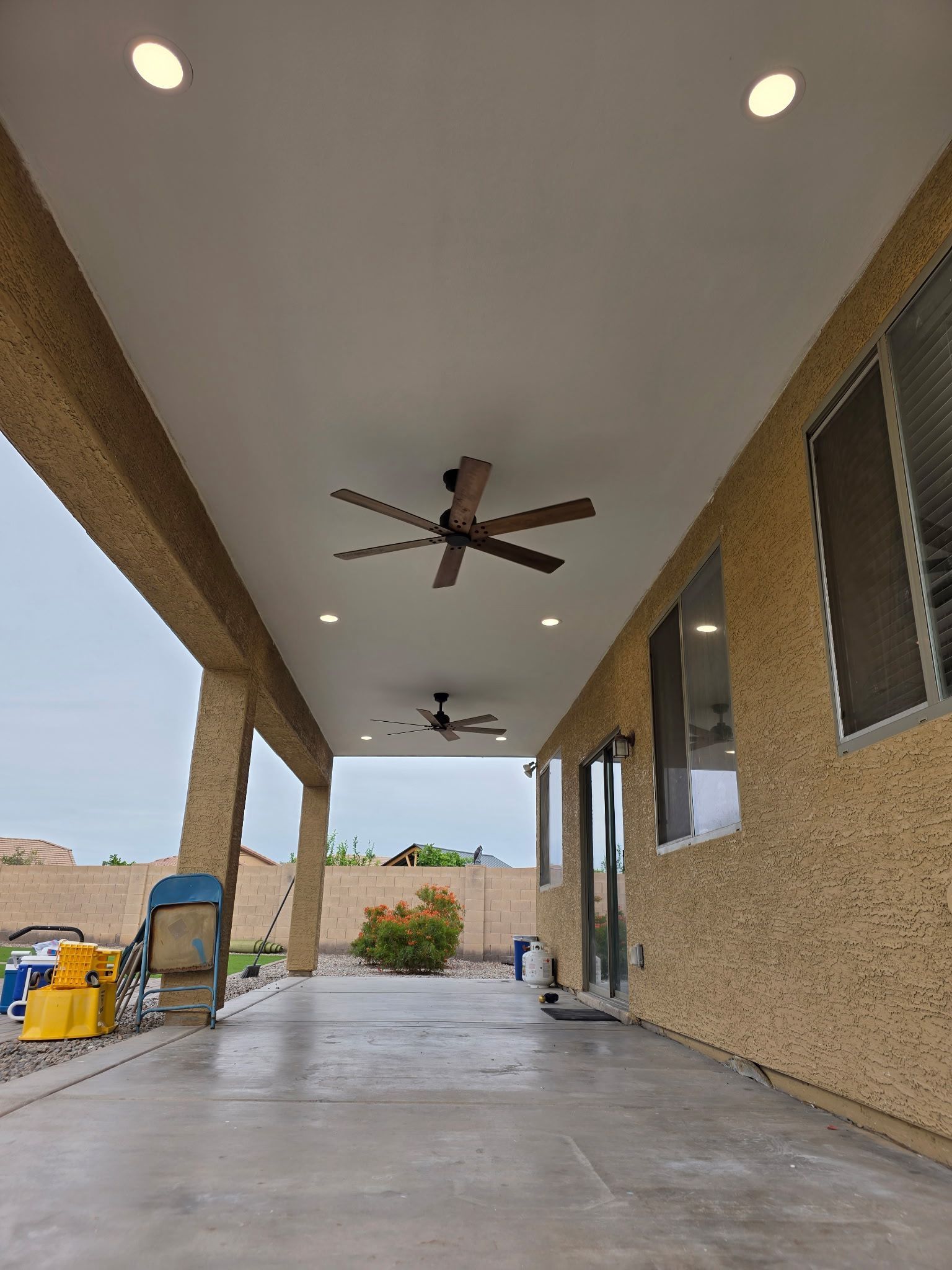 Covered patio with ceiling fans, concrete floor, brick columns, and a view of the yard and driveway.