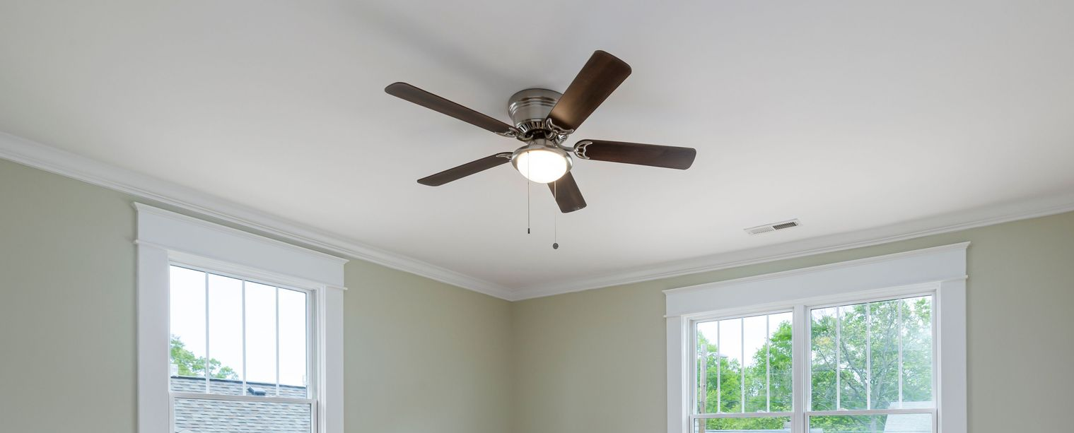 Bright bedroom ceiling with a lit fan, white trim, and two windows showing greenery outside