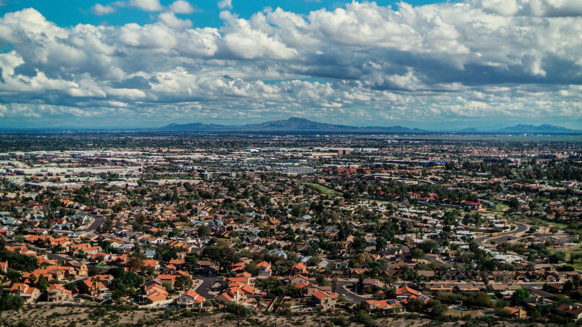 Panoramic cityscape of San Tan Valley with dense neighborhoods, distant mountains, and a cloudy sky