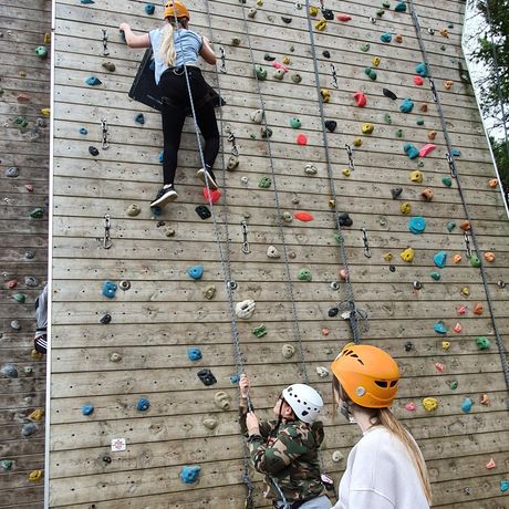 A woman is watching a child climb a climbing wall.