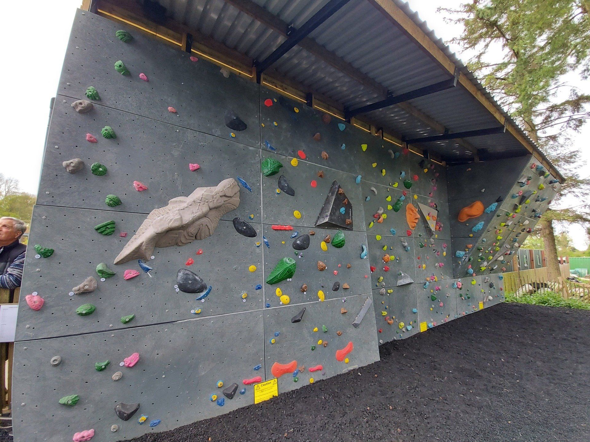 A man is standing in front of a large climbing wall.