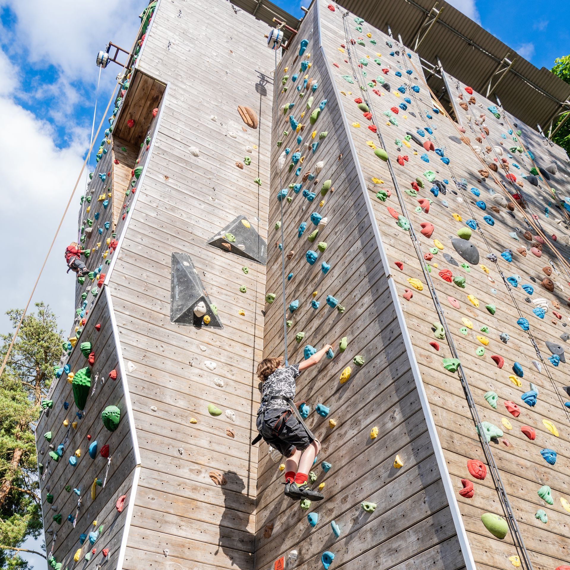 A man is climbing up a climbing wall while a woman watches