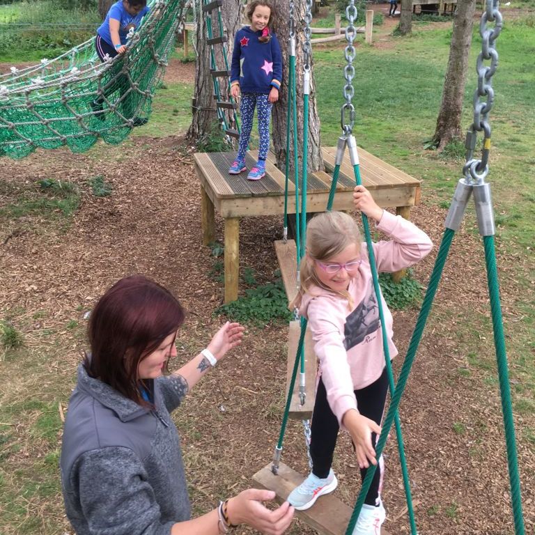 A woman is standing next to a girl on a swing.
