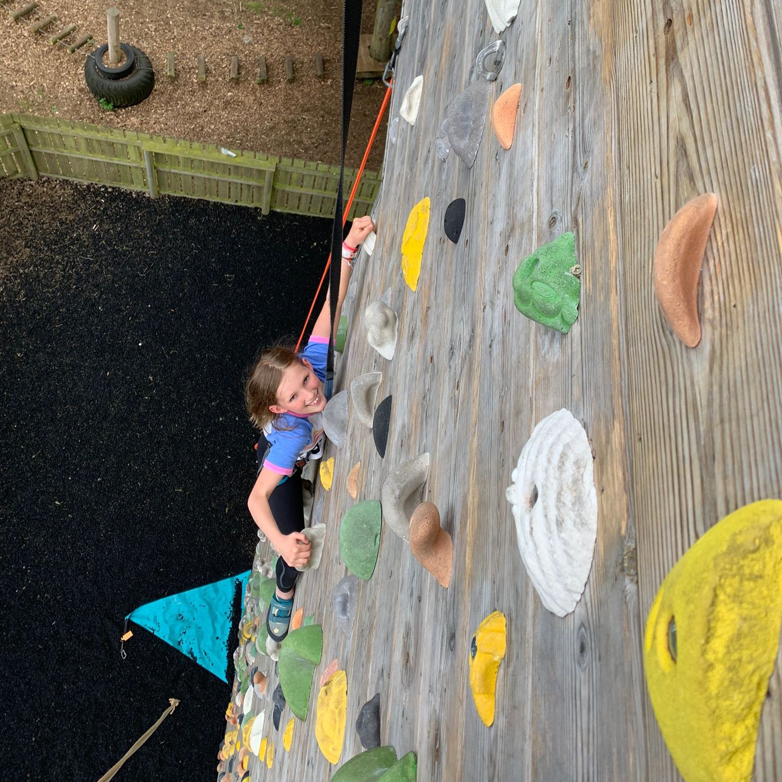 A young girl is climbing up a climbing wall