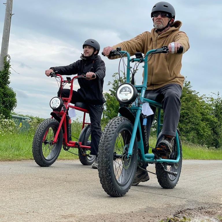 Two men wearing helmets are riding bicycles on a road