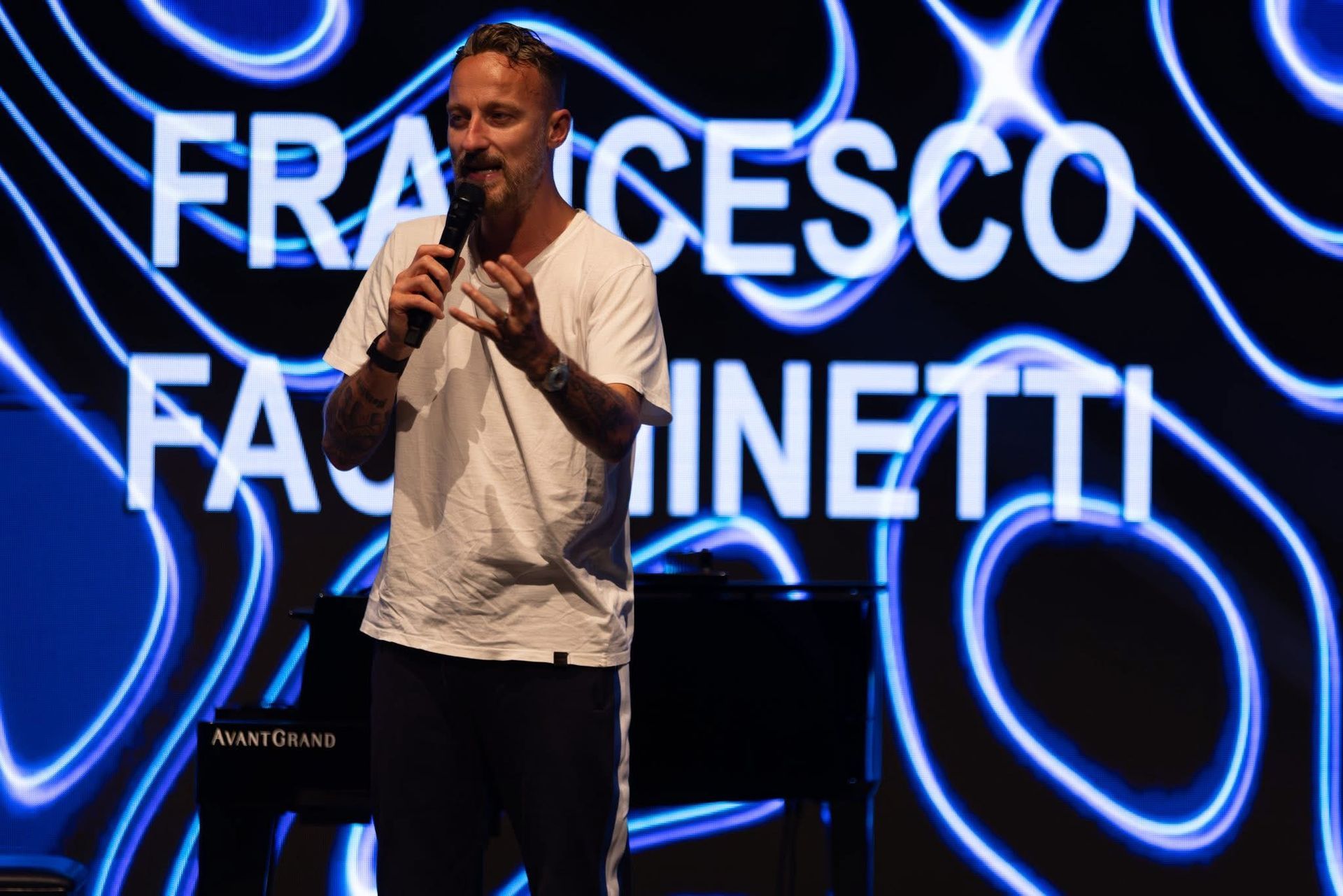 Un uomo parla sul palco con un'insegna al neon 