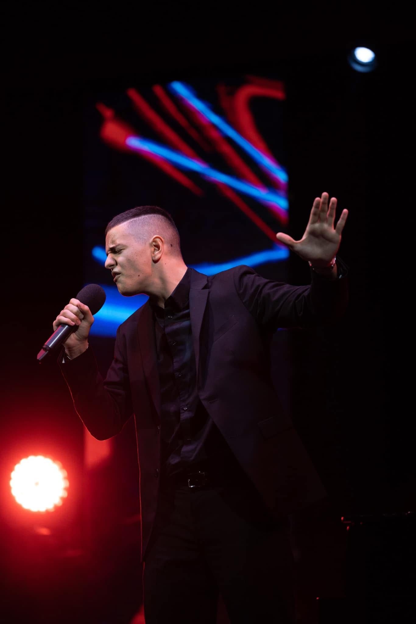 Cantante che tiene in mano un microfono su un palco buio illuminato da luci rosse e blu.