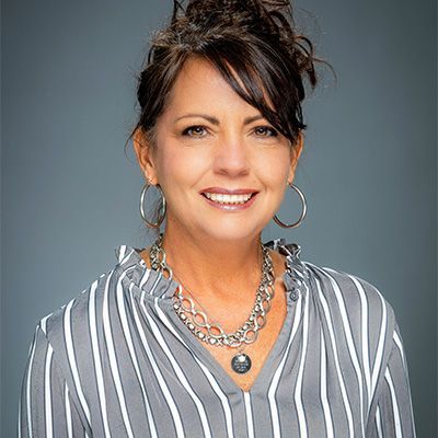 A woman wearing a striped shirt and a necklace is smiling for the camera.