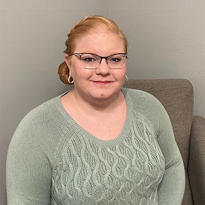 A woman wearing glasses and a green sweater is sitting in a chair.