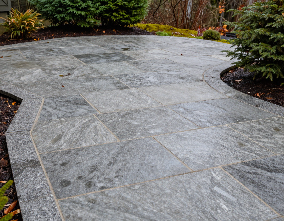 Curved gray stone patio bordered by mulch and plants in a landscaped yard